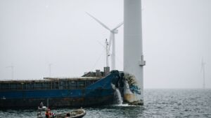 Torn bow plating on a freighter beside a wind turbine tower