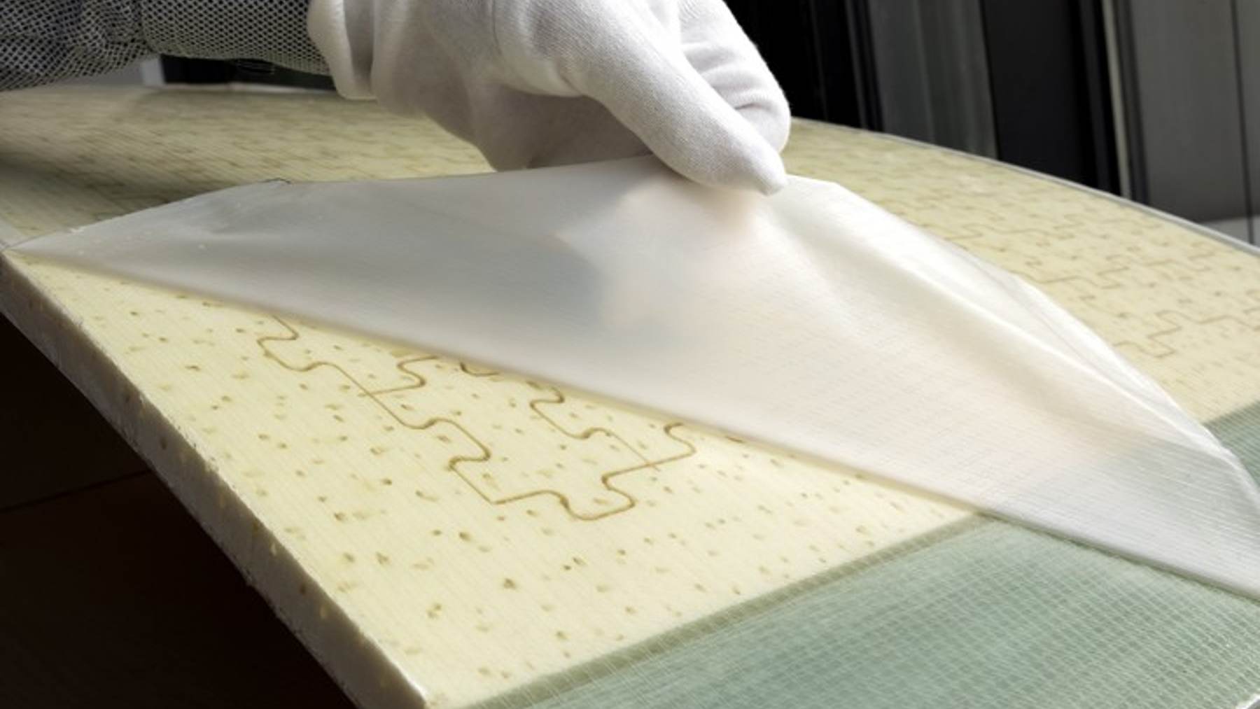 Hands peel a replaceable plastic leading edge off a wind turbine blade segment in a lab