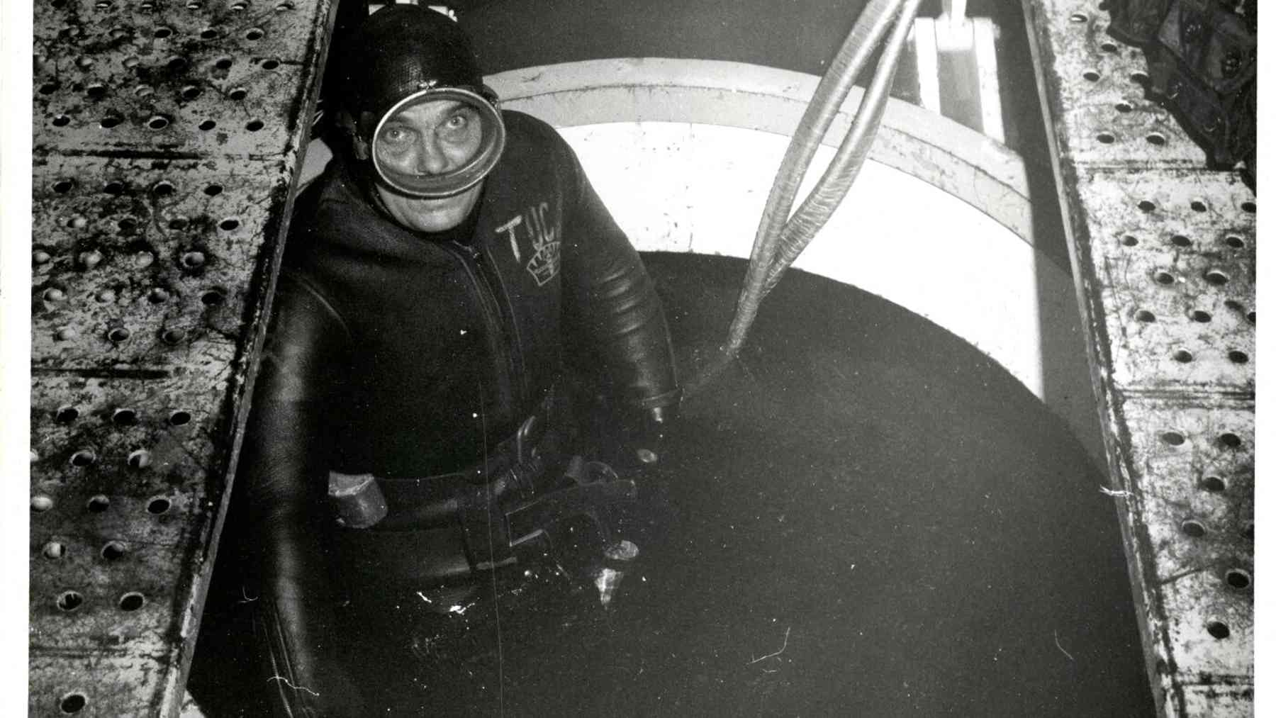 Diver inside the steel habitat 205 feet underwater keying a microphone handset, steel habitat held