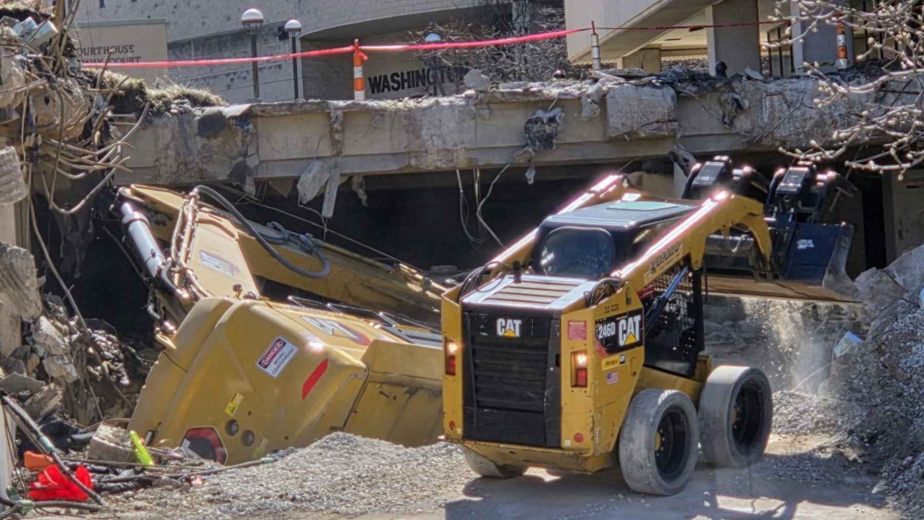 An excavator on its side in a collapsed parking garage basement